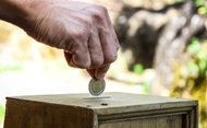 Hand wirft Münze in Opferstock