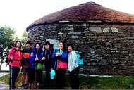 A group of girls in trekking gear standing in front of a stone hut.