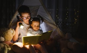 Siblings reading together at night by flashlight