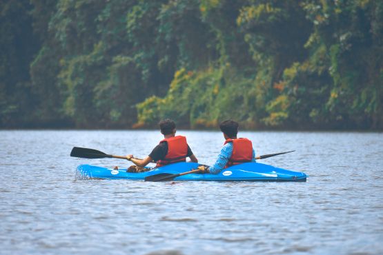 Deux jeunes hommes avancent dans un lac sur un kayak vers des arbres au fond.