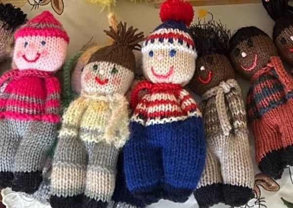 A group of handmade knitted dolls, with various skin tones and colorful outfits, featuring embroidered smiles and hats.