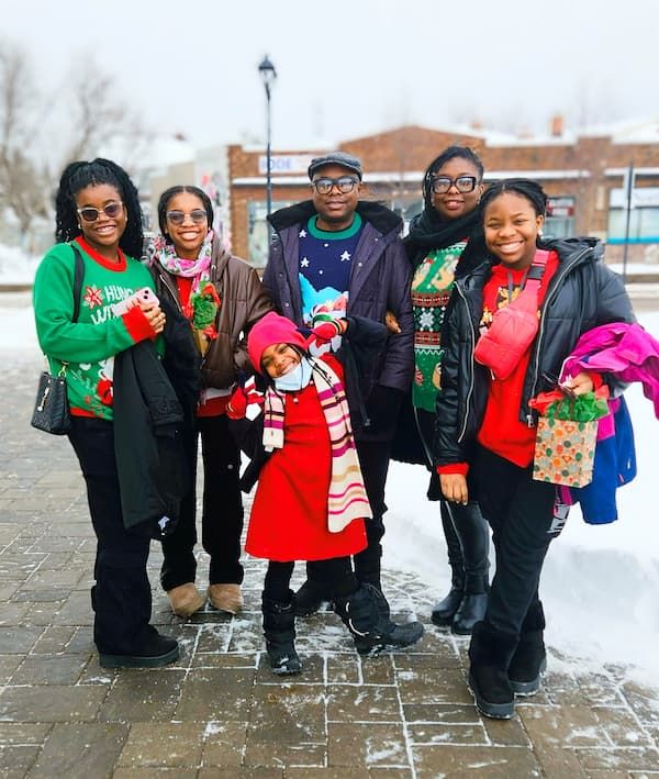 Family of 6 posing for the camera wearing colorful Christmas sweater.