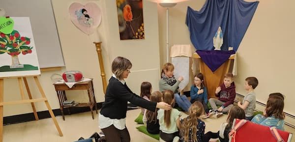 Groupe d'enfants assis au sol en cercle sur des coussins verts recevant de la formation à la vie chrétienne.