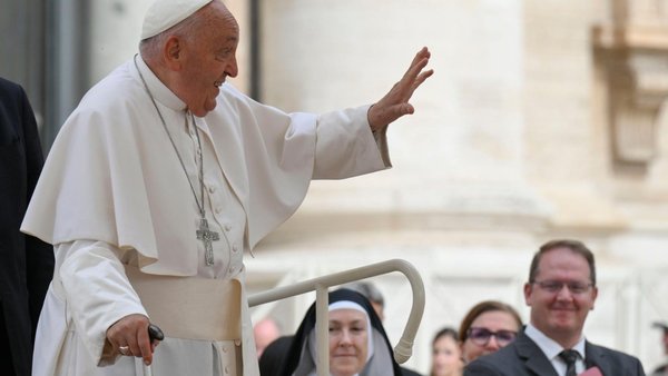 Side view of Pope Francis standing on a moving Pope mobile with the aid of a cane