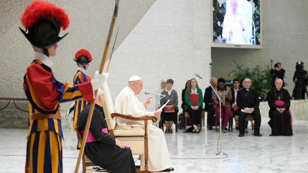 Pope Francis seated on a podium flanked by two Swiss guards, view from the right