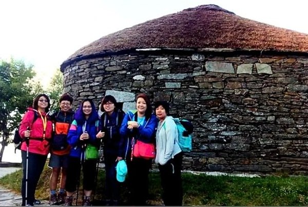 A group of girls in trekking gear standing in front of a stone hut.